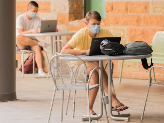 male student sitting at an outdoor table wearing a mask